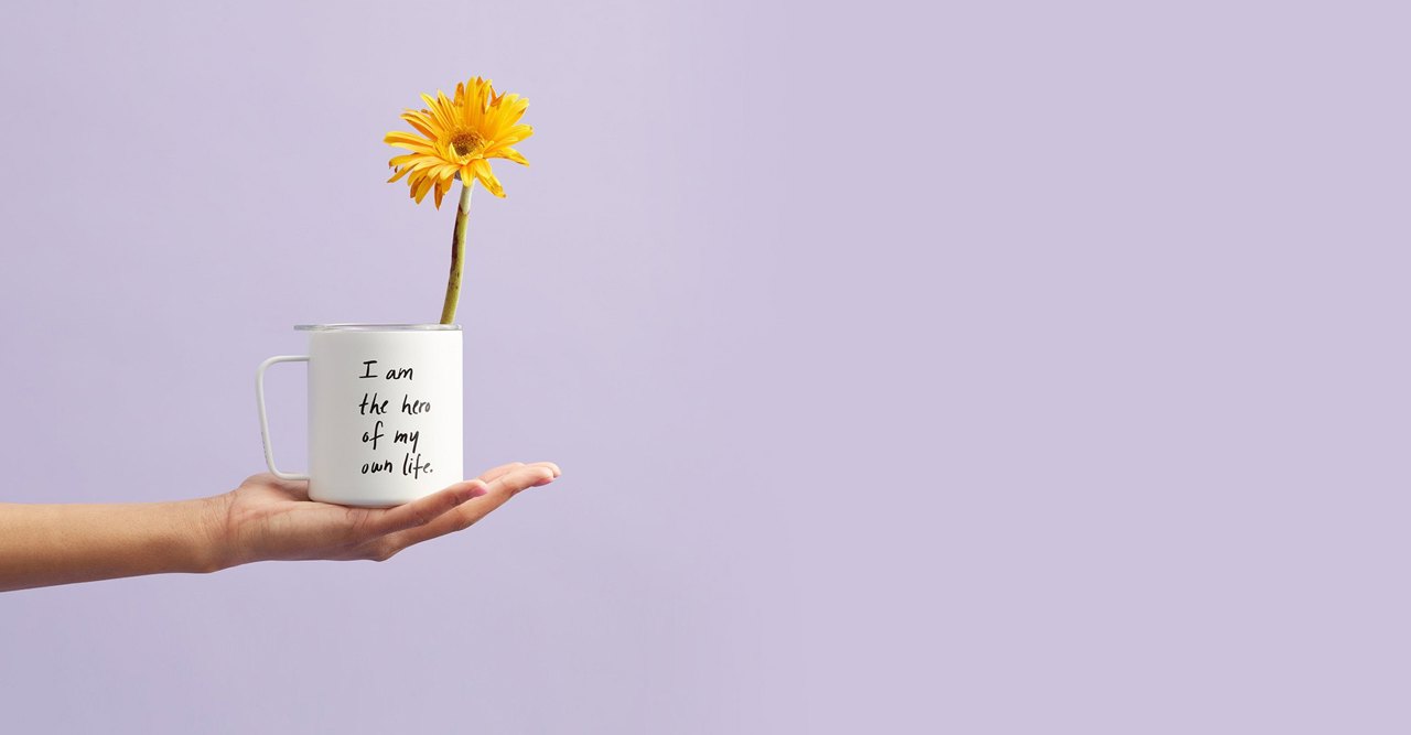 A hand holding a mug that reads: I am the hero of my own life